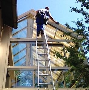 Fensterputzer steigt auf hohe Leiter, um Wintergarten zu putzen